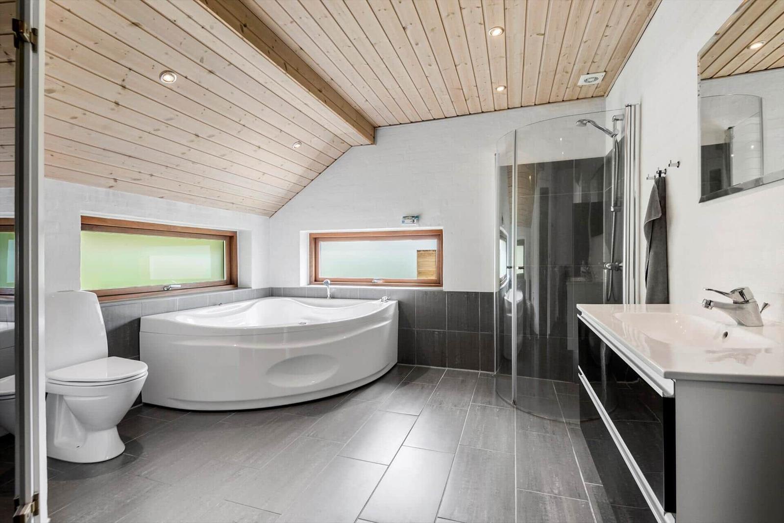 Badezimmer mit Whirlpool, Dusche und Waschbecken unter Holzdecke.