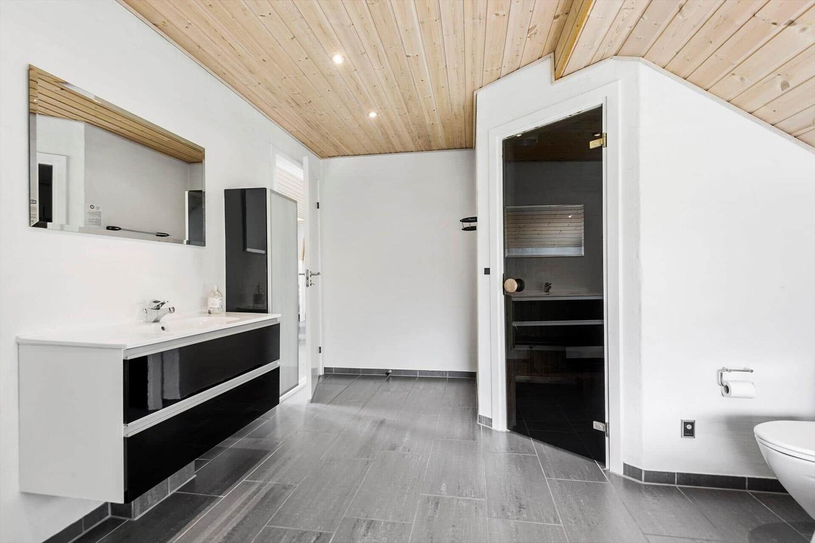 Badezimmer mit Waschtisch, Spiegel und Dusche. Holzdecke und graue Fliesen.