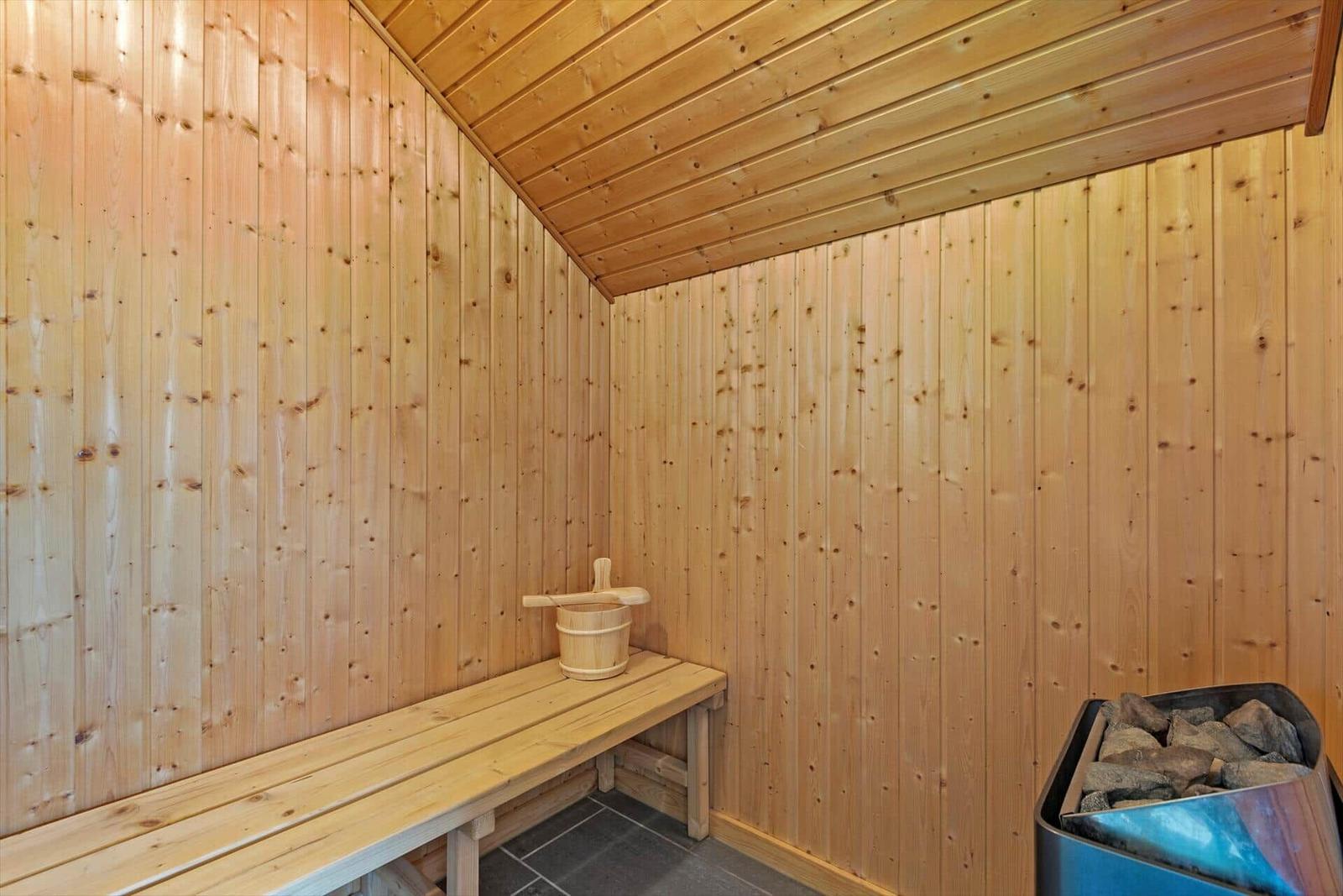 Sauna mit Holzwandverkleidung, Sitzbank und Steinofen mit Holzbucket.