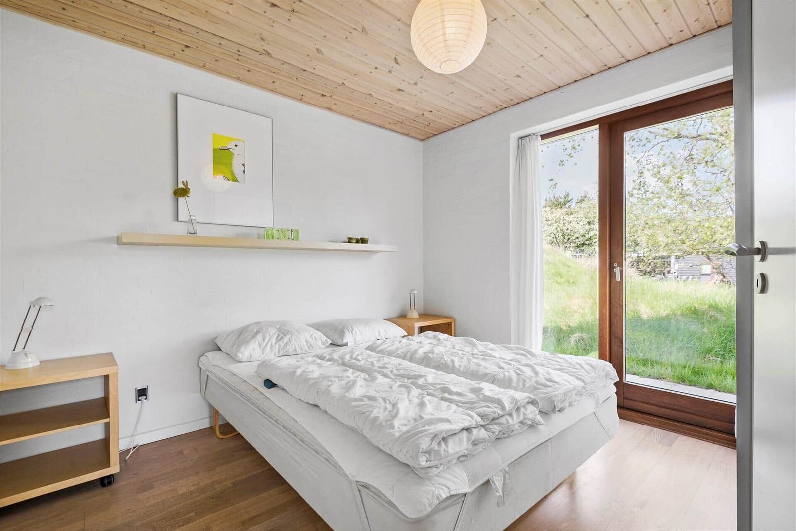 Schlafzimmer mit Bett, Holzdecke und Fenster zur grünen Außenseite.