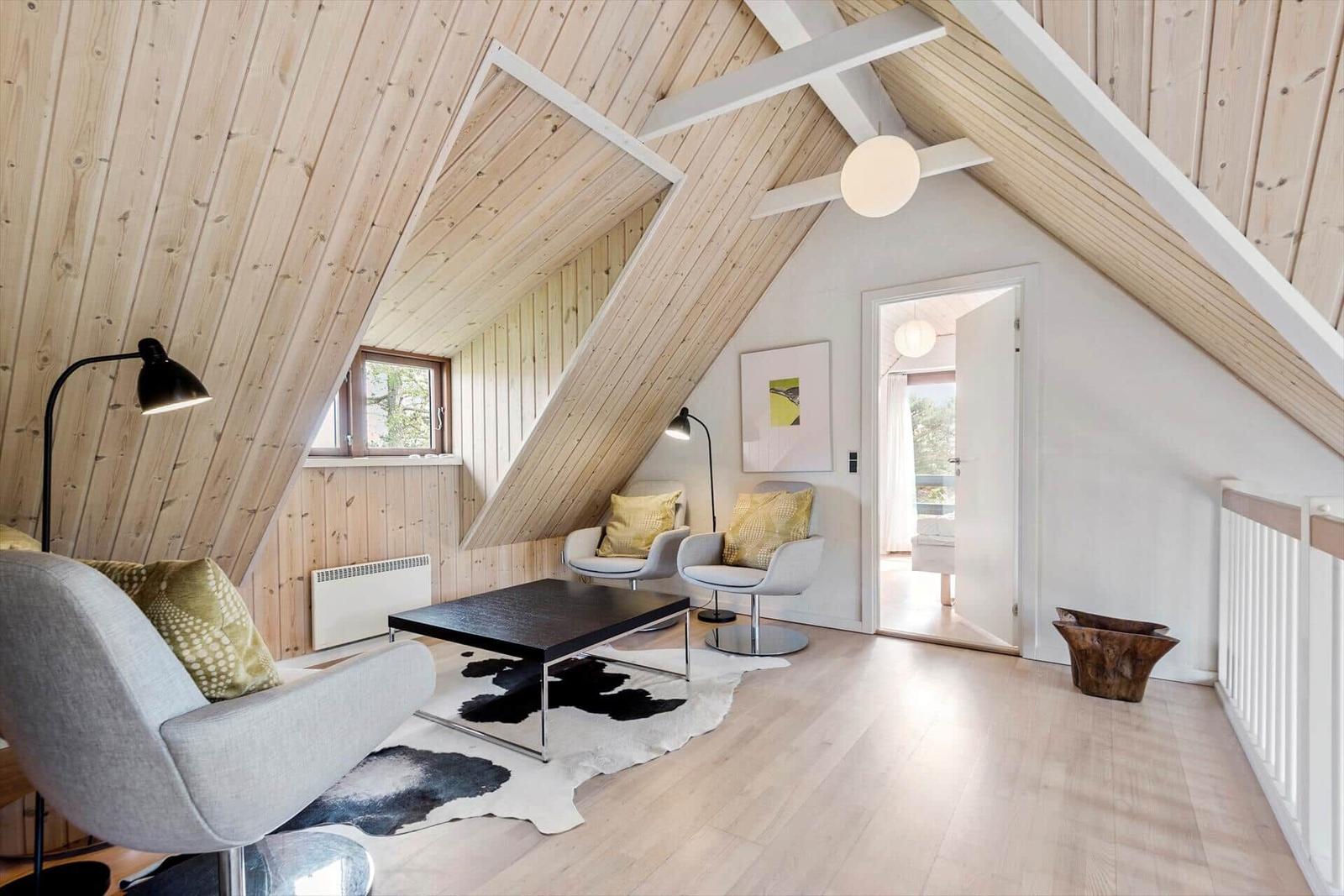 Wohnzimmer mit Holzdecke, zwei Sesseln, Tisch und Fellteppich.