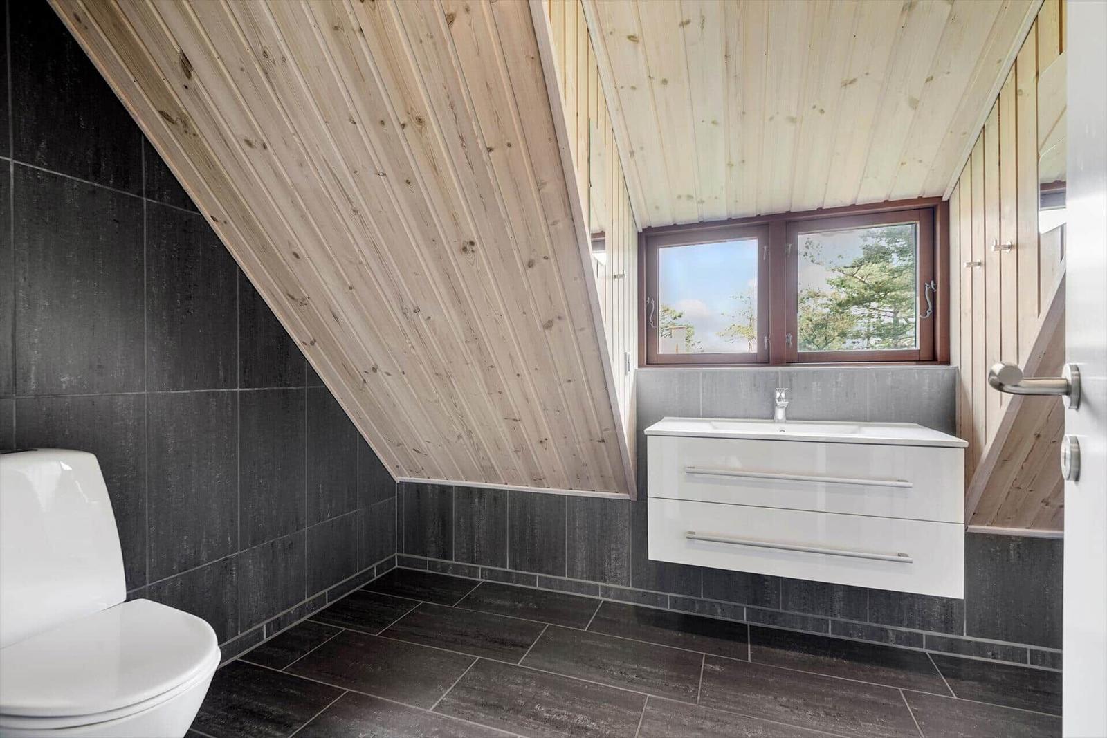 Badezimmer mit Holzdecke, Toilette und Waschbecken mit Fenster.