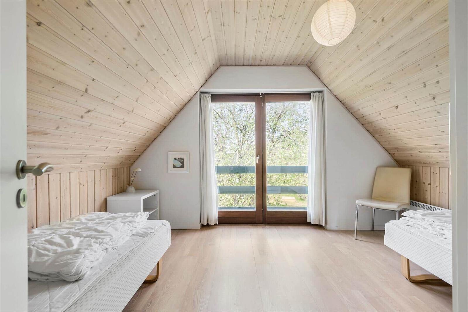 Zimmer mit zwei Betten, Holzdecke und Fenster zum Balkon.