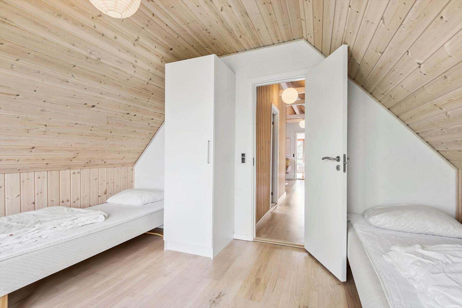 Zwei Einzelbetten in einem Dachzimmer mit Holzwand und -decke. Eine Tür führt in den Flur.