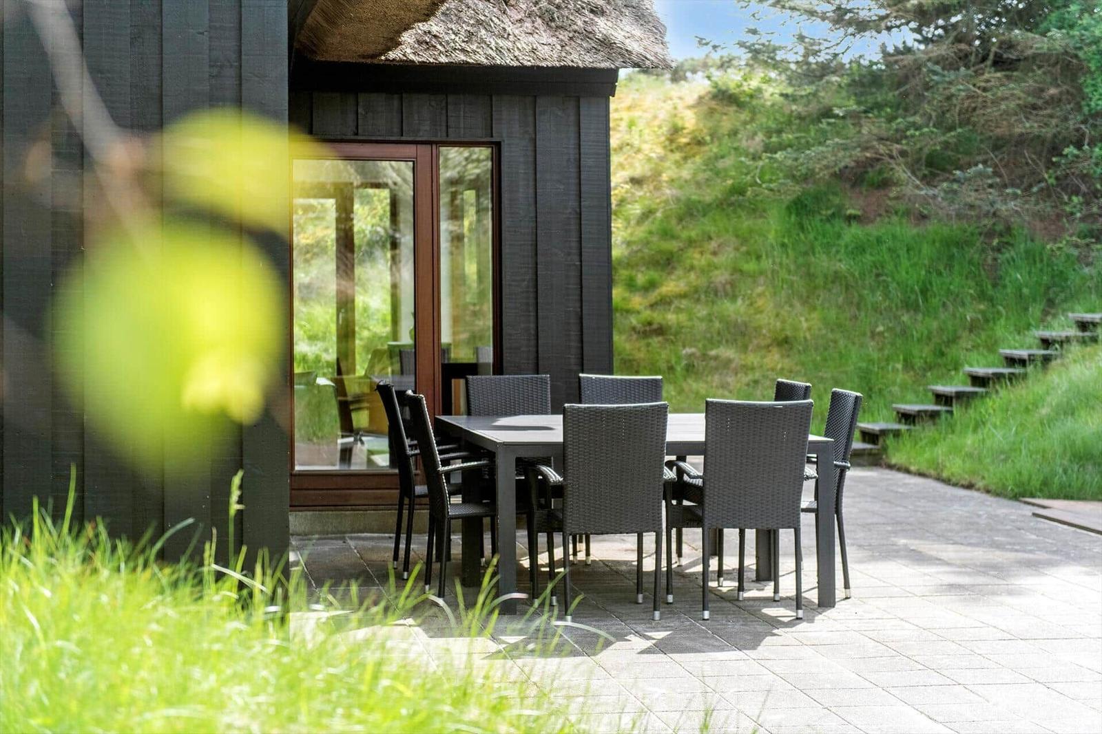 Terrasse mit Tisch und Stühlen vor einem Haus mit Schiebetür und Dach aus Stroh.