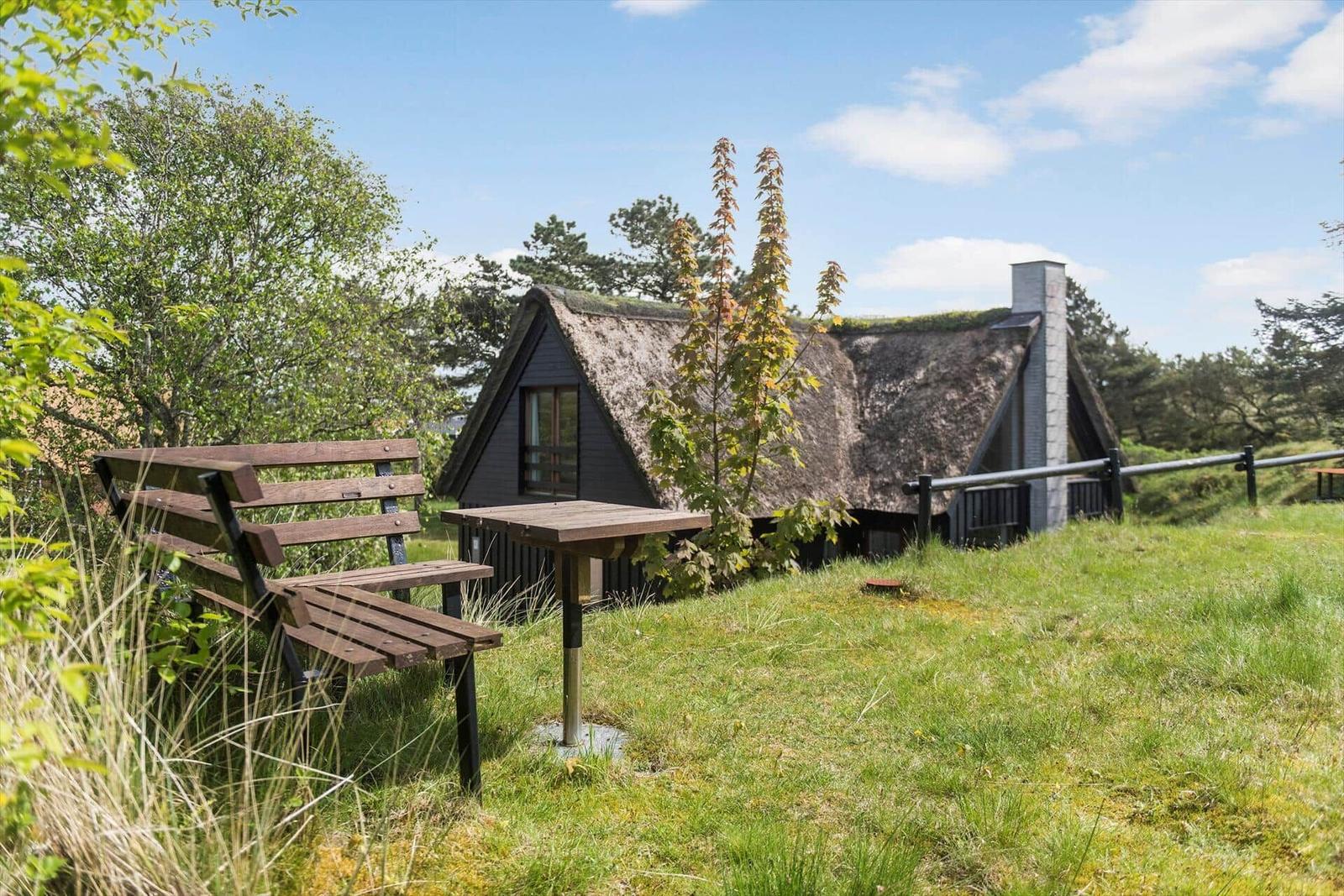 Hütte mit grasbedecktem Dach, Holztisch und Bank im Gras