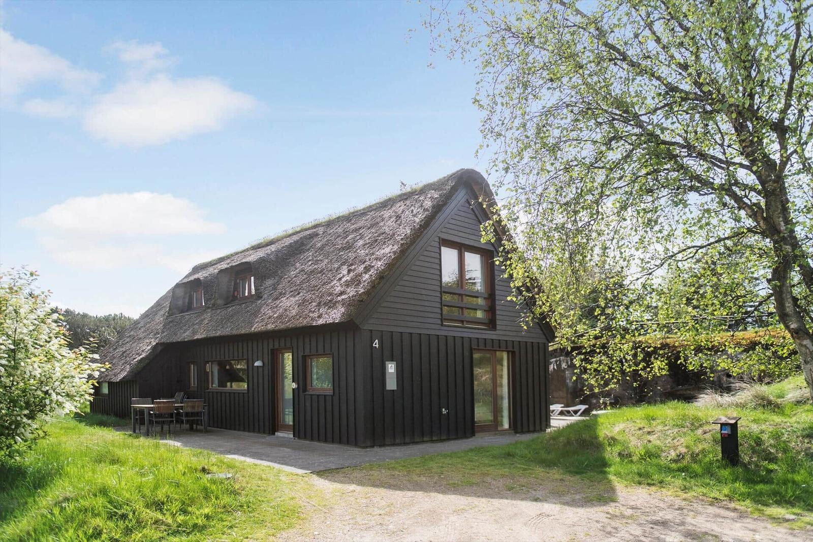 Haus mit strohgedecktem Dach, Holzfassade und Gartenbereich mit Tisch und Stühlen.