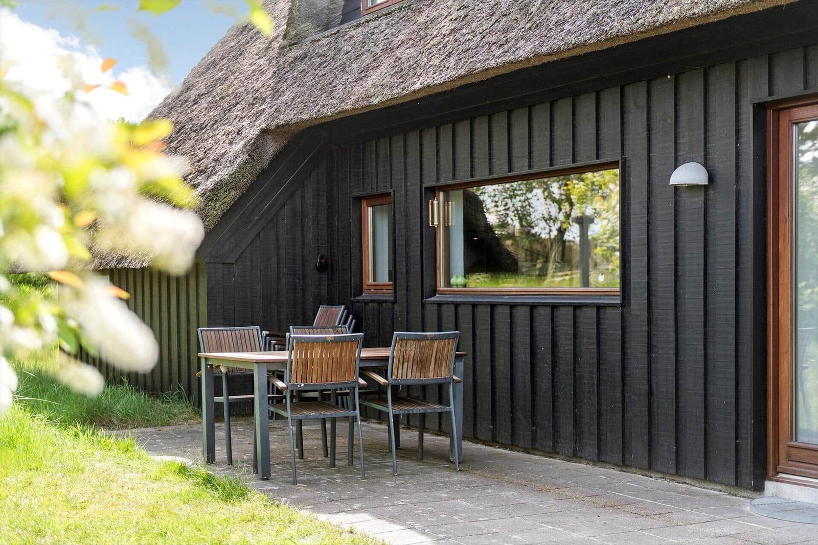 Haus mit Strohdach und Holzfassade. Außentisch mit Stühlen auf Steinplatten.
