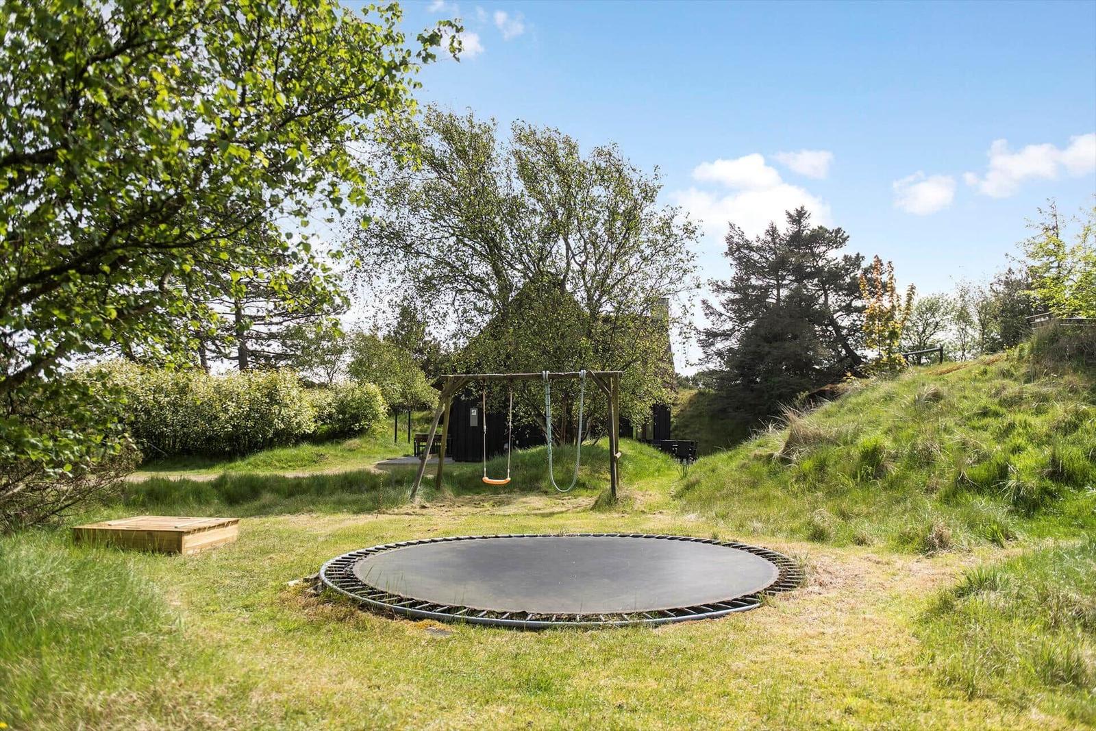 Runder Trampolin im Garten mit Schaukel und Bäumen.