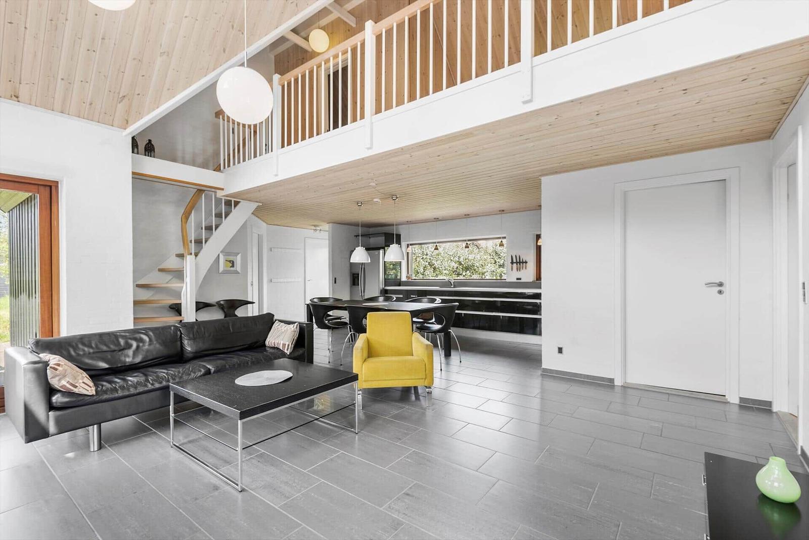 Wohnbereich mit Sofa, gelber Sitzgelegenheit und Essbereich unter offener Holzdecke.