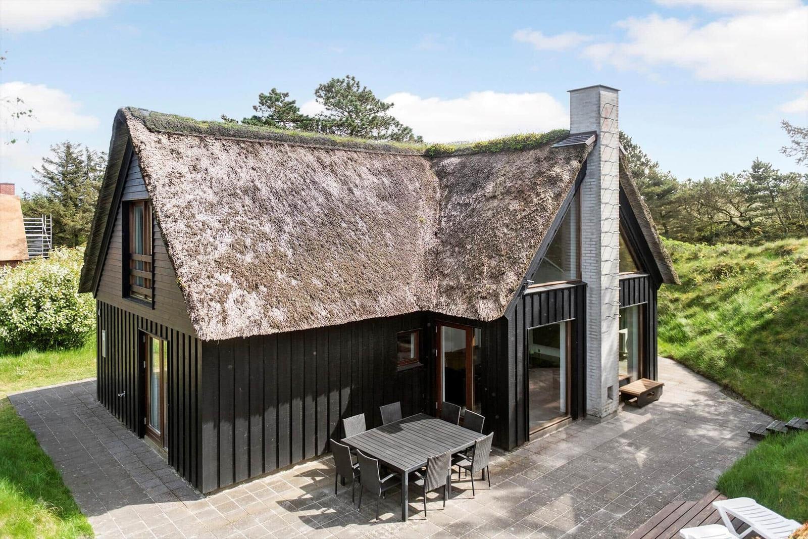 Haus mit Grasdach, Terrasse und Sitzgruppe im Freien.