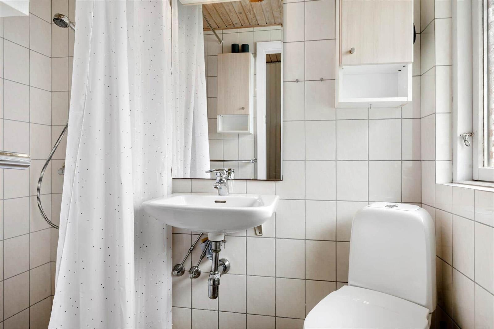 Badezimmer mit Dusche, Waschbecken und Toilette. Weiße Fliesen und Holzdecke.