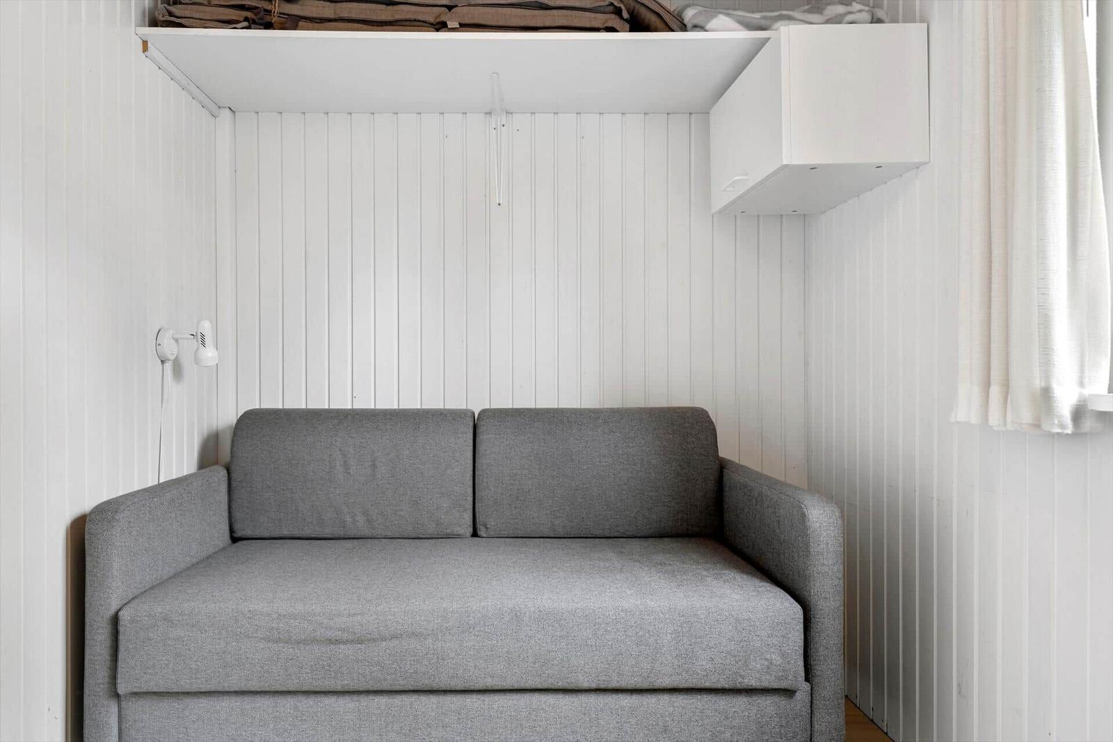 Ein grauer Sofa im Raum mit weißen vertikalen Wänden und einer Wandlampe.