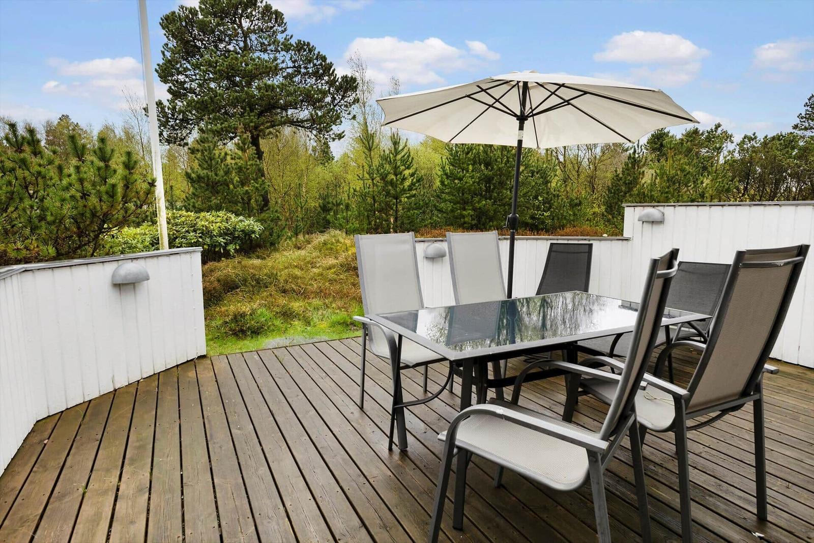 Terrasse mit Tisch, Stühlen und Sonnenschirm. Umgeben von Bäumen und Grün.