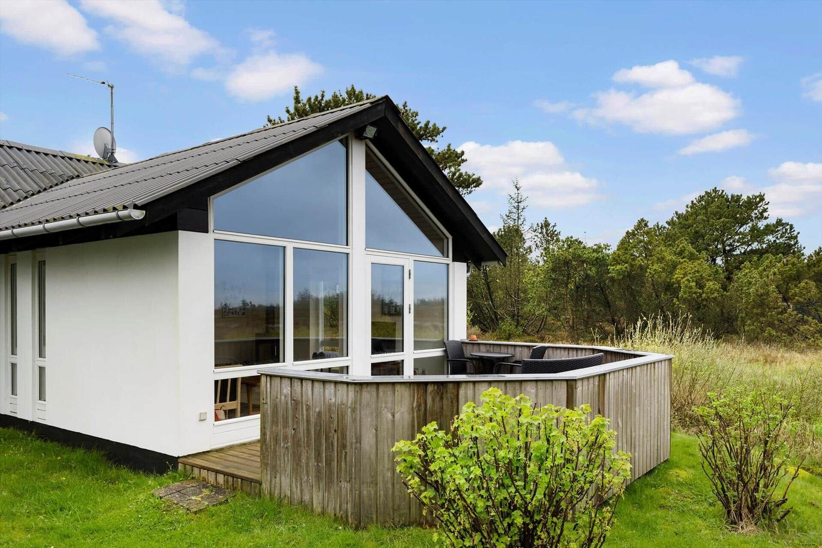 Moderne Unterkunft mit großem Fensterbereich und Holzterrasse in grüner Umgebung.
