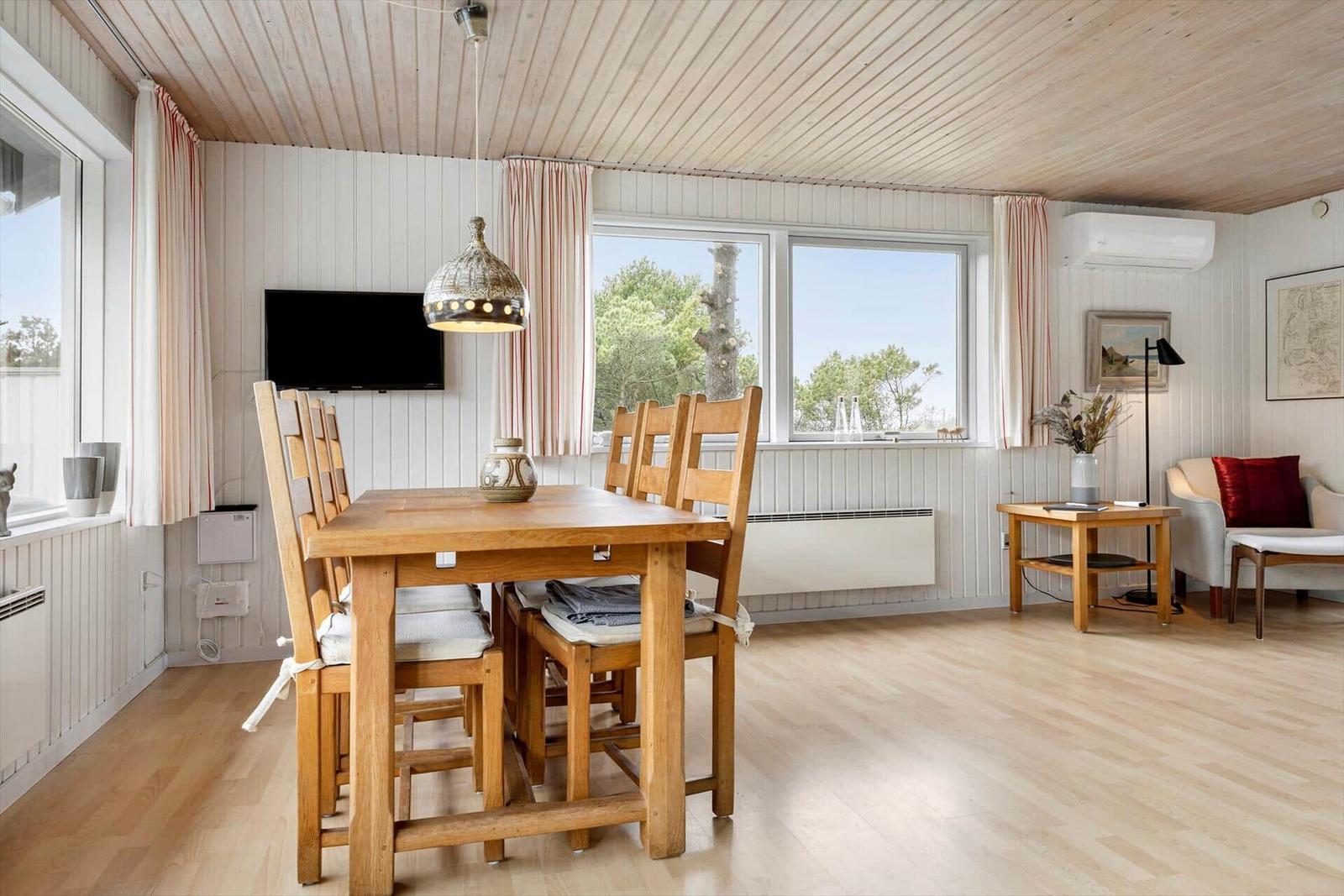 Essbereich mit Holztisch und Stühlen, Fernseher und Fenster mit Blick auf Bäume.