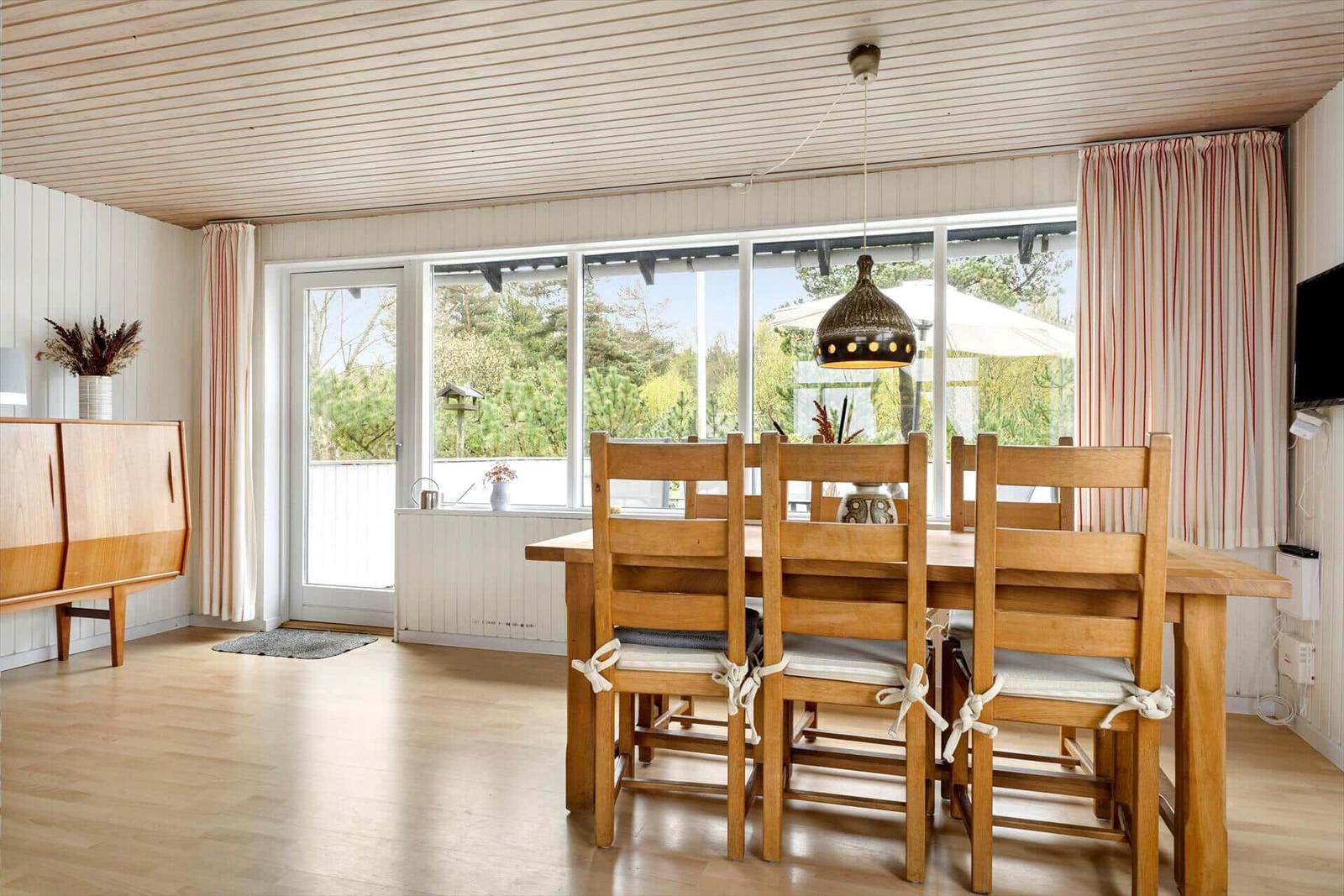 Esszimmer mit Holztisch, Stühlen und großen Fenstern. Holzdecke und Parkettboden.