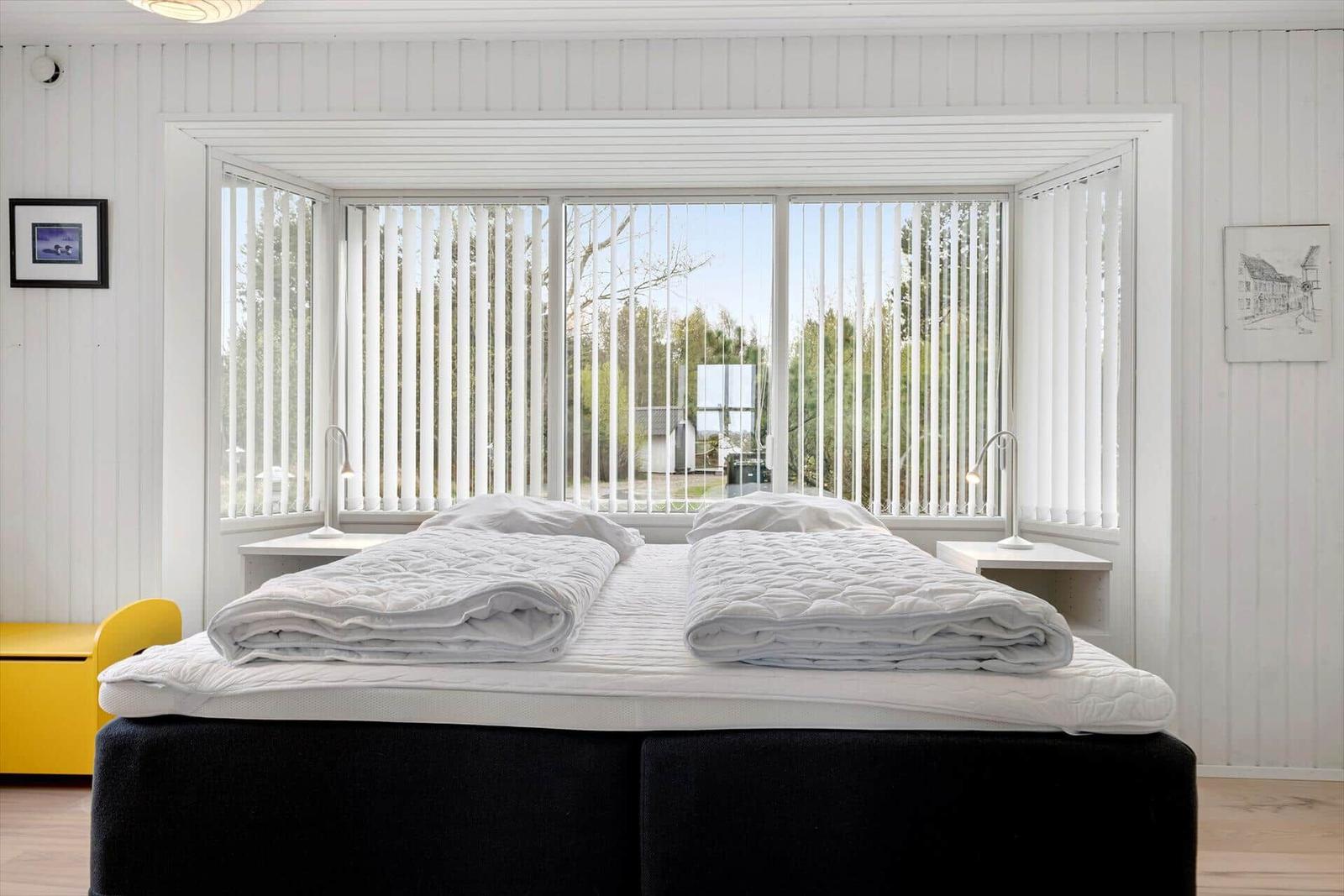 Schlafzimmer mit Doppelbett, Fenster und Nachttischen.