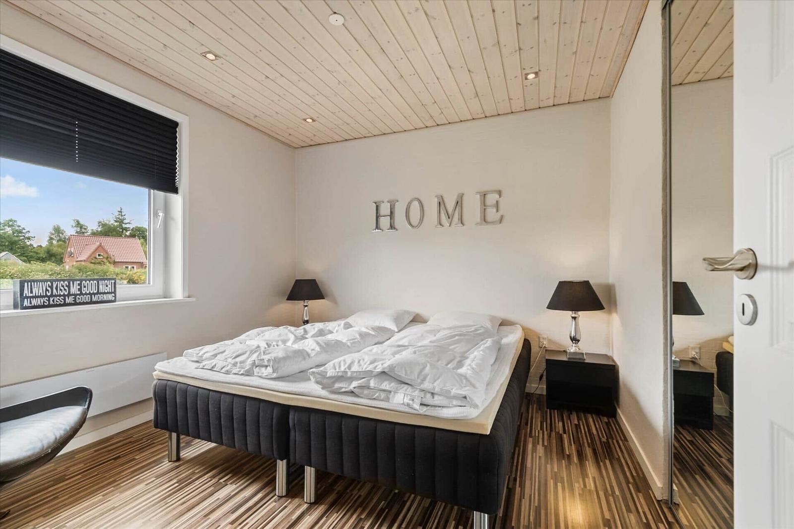 Schlafzimmer mit Bett, Nachttischen und Fenster. Wand mit Schriftzug HOME.