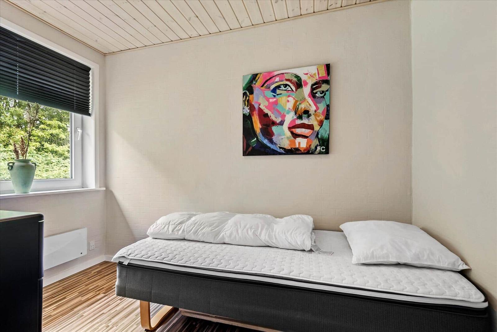 Schlafzimmer mit Bett, Wandbild und Fenster mit Blick auf Grün.