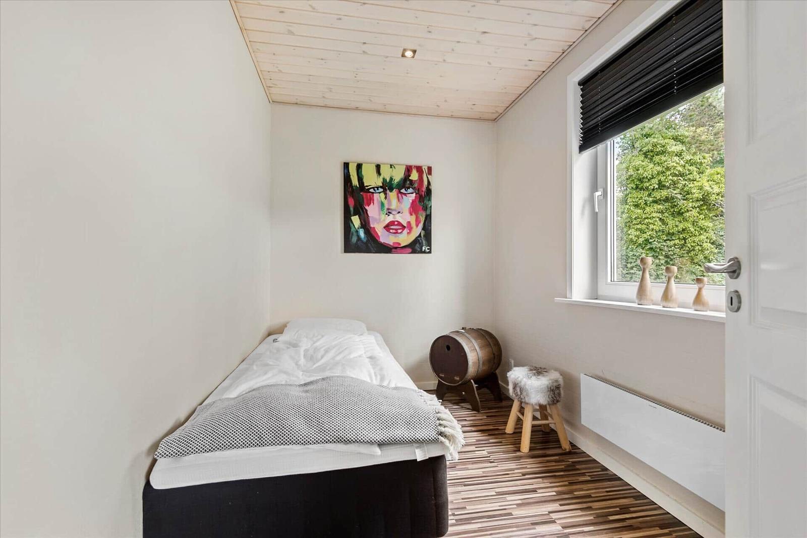 Ein Schlafzimmer mit Bett, Wandbild, Fenster und Holzboden.