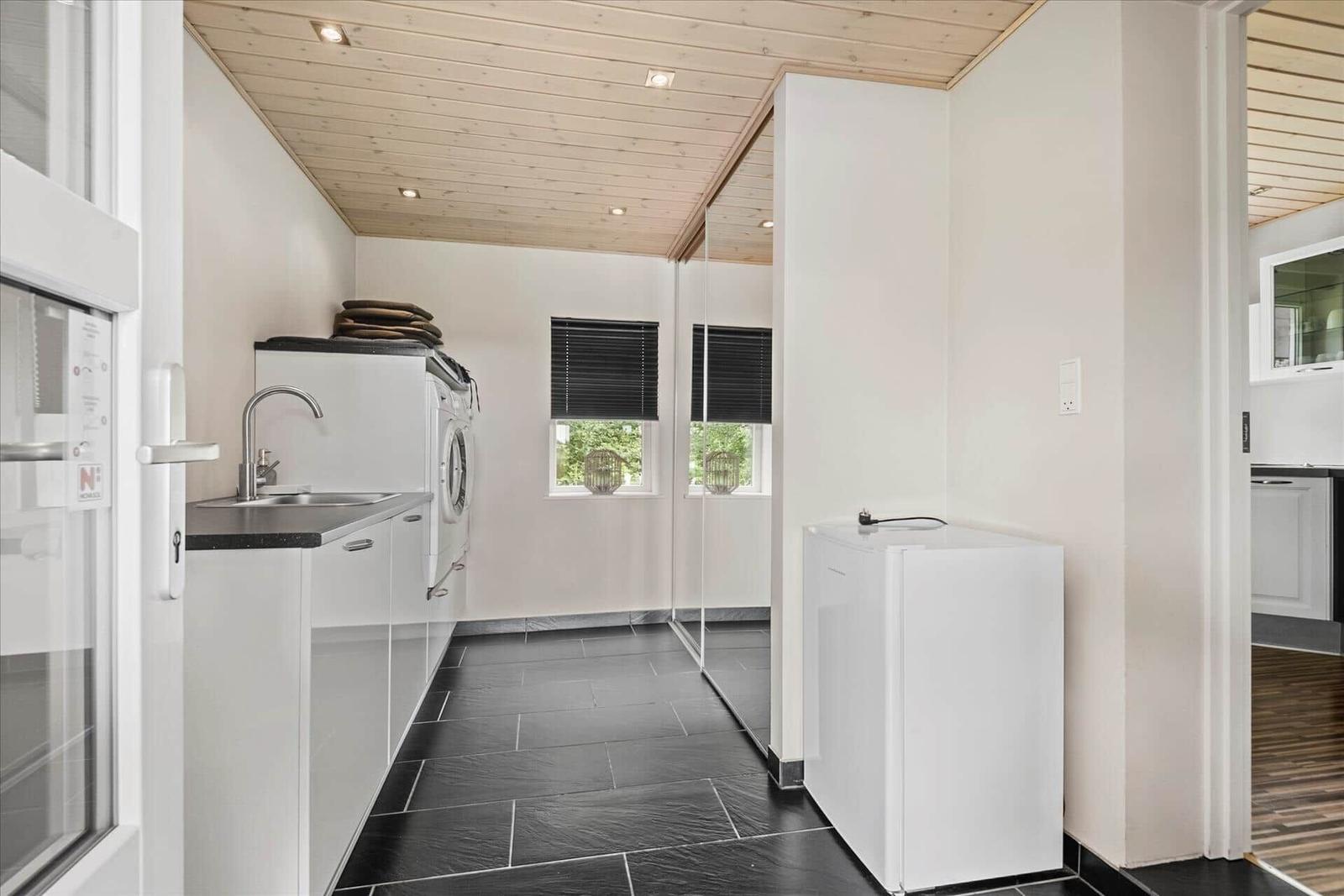 Wohnung mit Küchenzeile, Waschmaschine und Kühlschrank. Holzdecke und schwarze Fliesen.