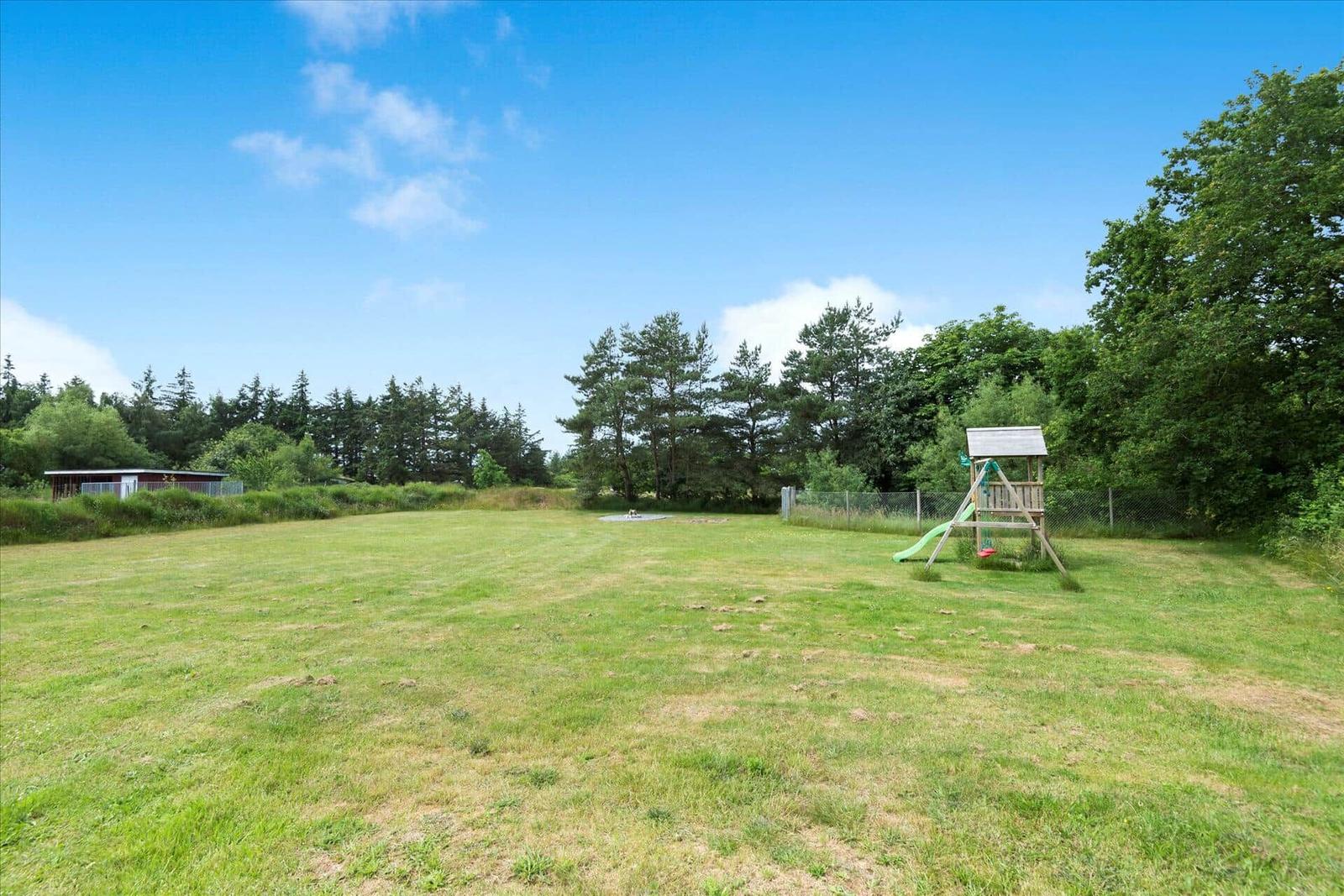 Großer grüner Garten mit Spielplatz und Wald im Hintergrund.