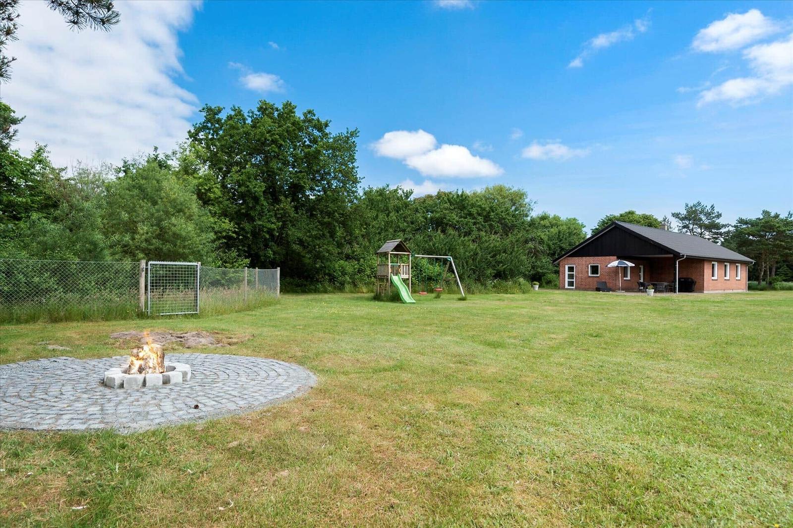 Haus mit Garten, Spielplatz und Feuerstelle unter blauem Himmel.
