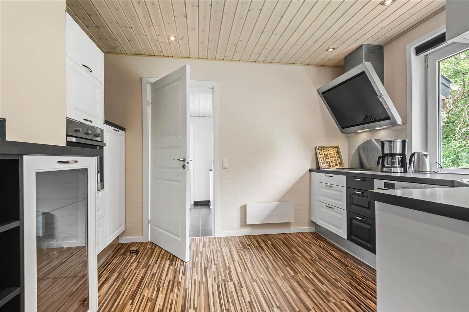 Küche mit weißen Schränken, Holzboden und Fensterblick auf Grün.