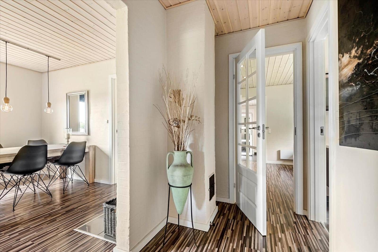 Eingangsbereich mit Holzboden, grünem Vasenobjekt und Blick in Esszimmer und Wohnbereich.