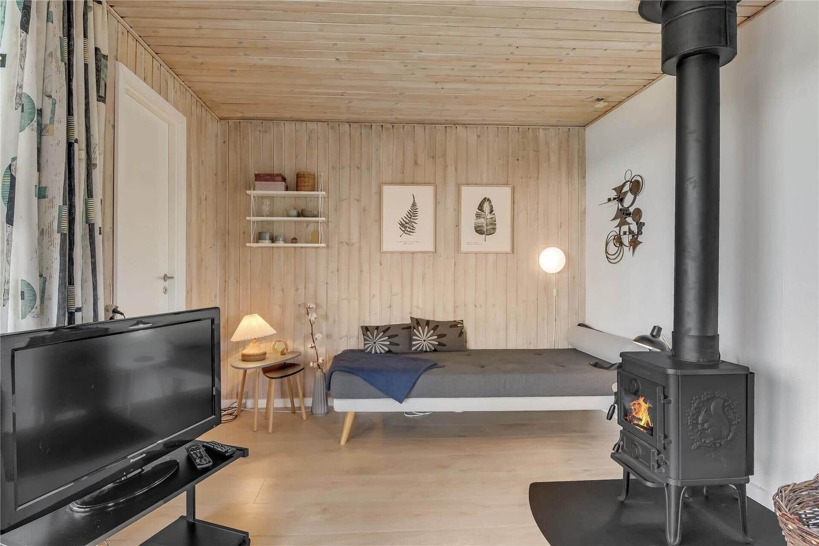 Ein Raum mit Bett, Kaminofen und Fernseher. Holzwände und -decke. Wandbilder und Beleuchtung.