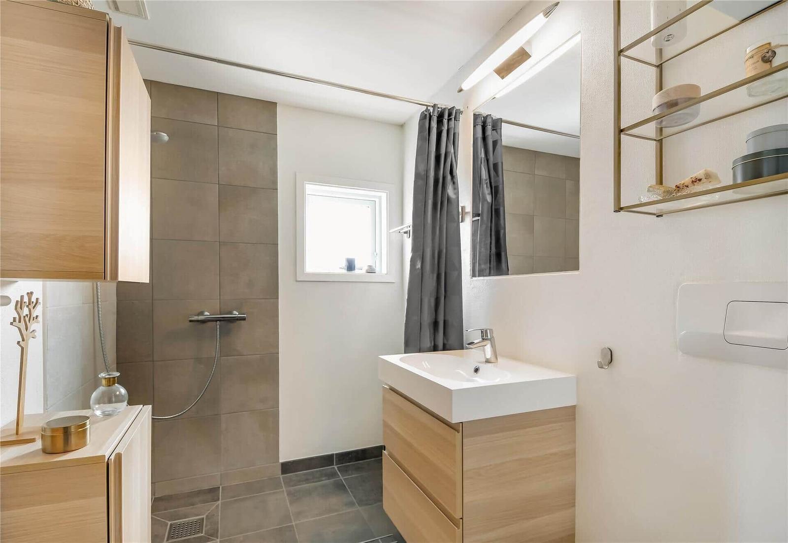 Bad mit Dusche, Waschbecken und Spiegel. Holzmöbel und goldene Regale.