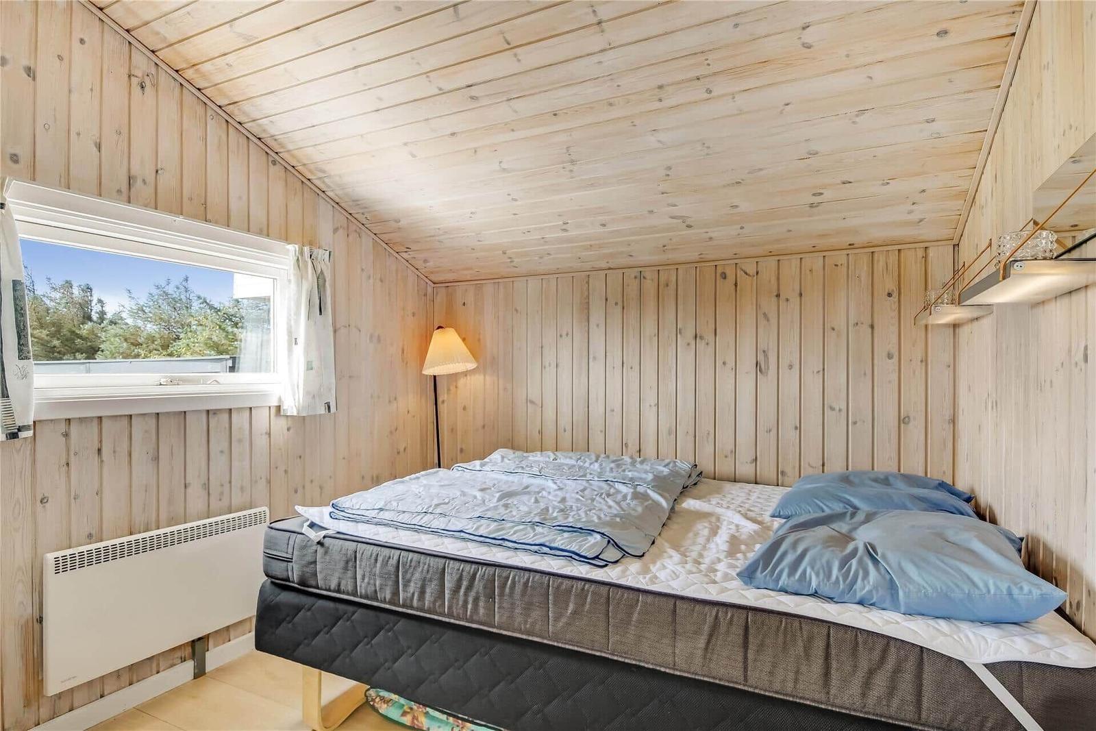 Schlafzimmer mit Holzwand, Bett, Fenster und Stehlampe.