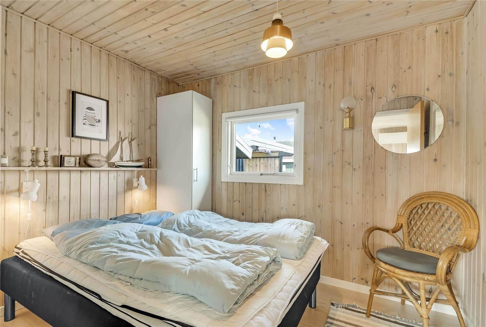 Schlafzimmer mit Holzwand, Bett, Stuhl und Fenster