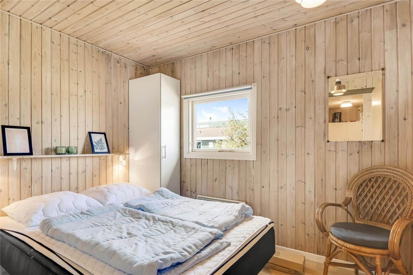 Schlafzimmer mit Holzwand, Bett, Stuhl und Fenster.