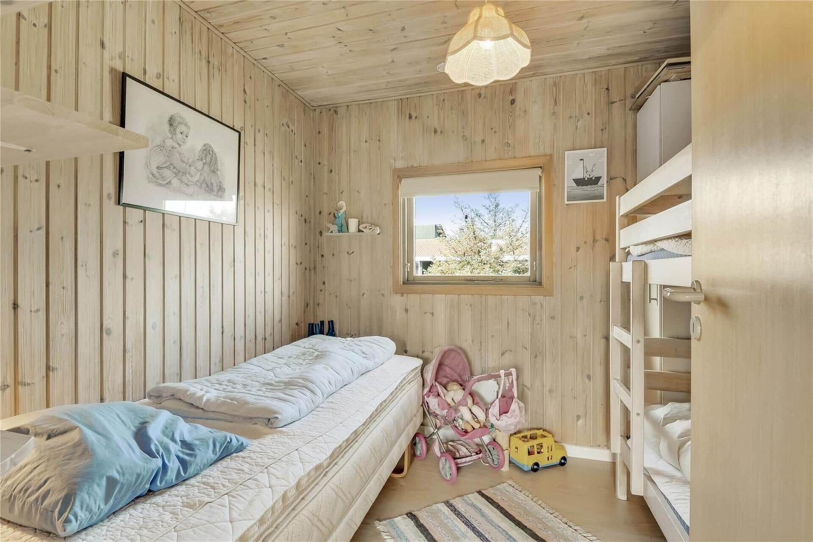 Ein Schlafzimmer mit Holzwand, Bett, Krippenbett, Fenster und Spielzeug.