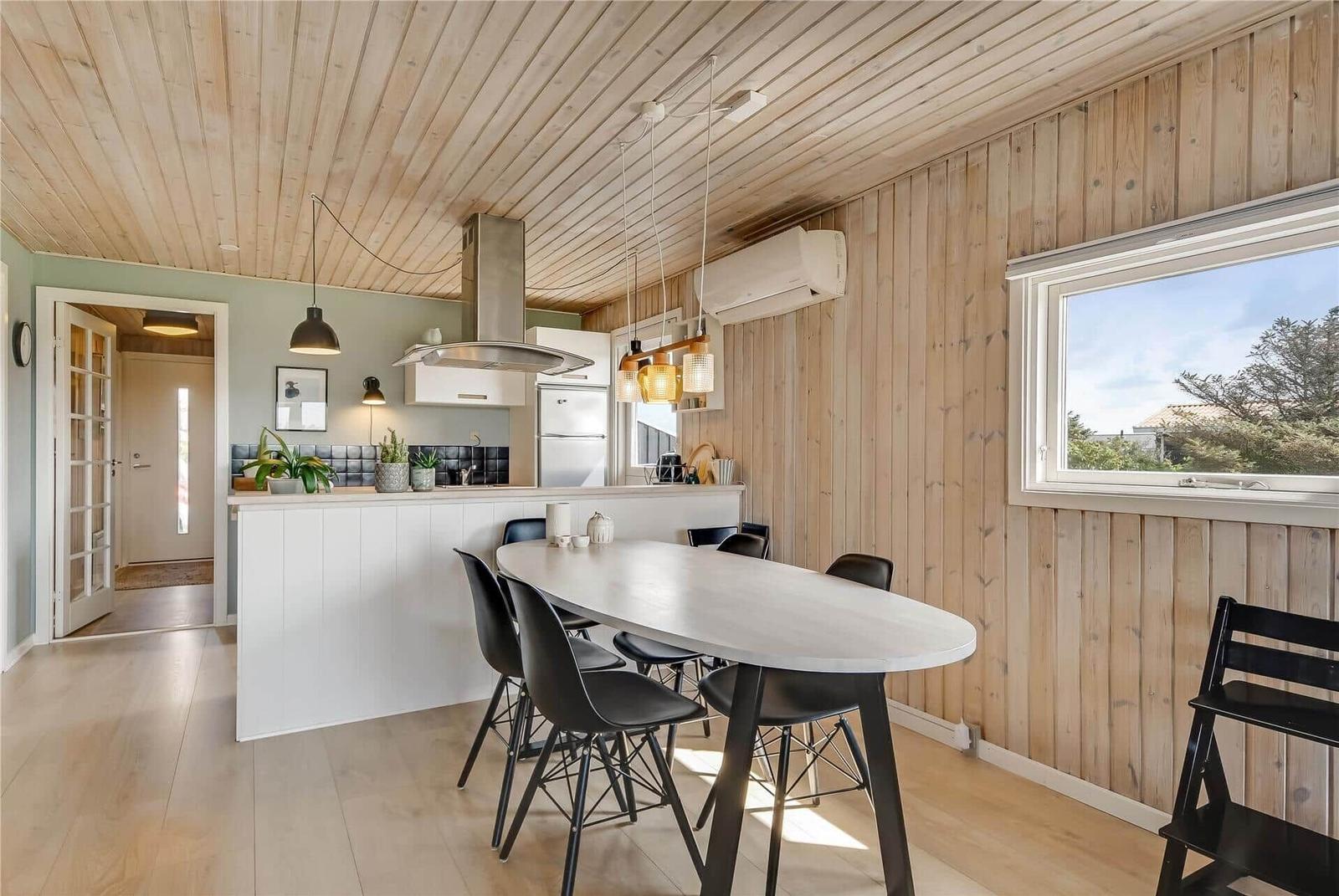 Küche mit Essbereich, Holzwand und -decke, weißer Arbeitsplatte und schwarzen Stühlen.