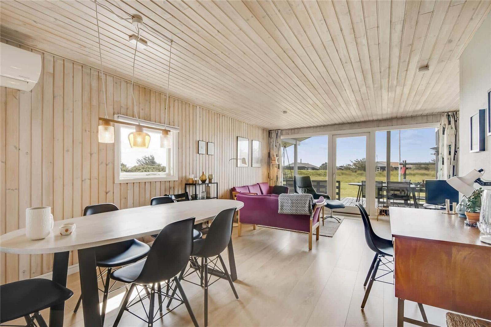 Wohn- und Essbereich mit Holzwand, Tisch, Stühlen und Sofa. Blick auf Außenbereich.