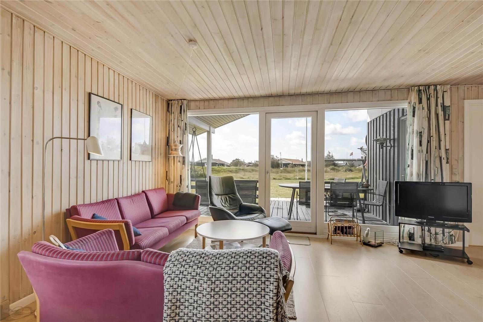 Wohnzimmer mit rosa Sofa, Fernseher und Blick auf die Terrasse.