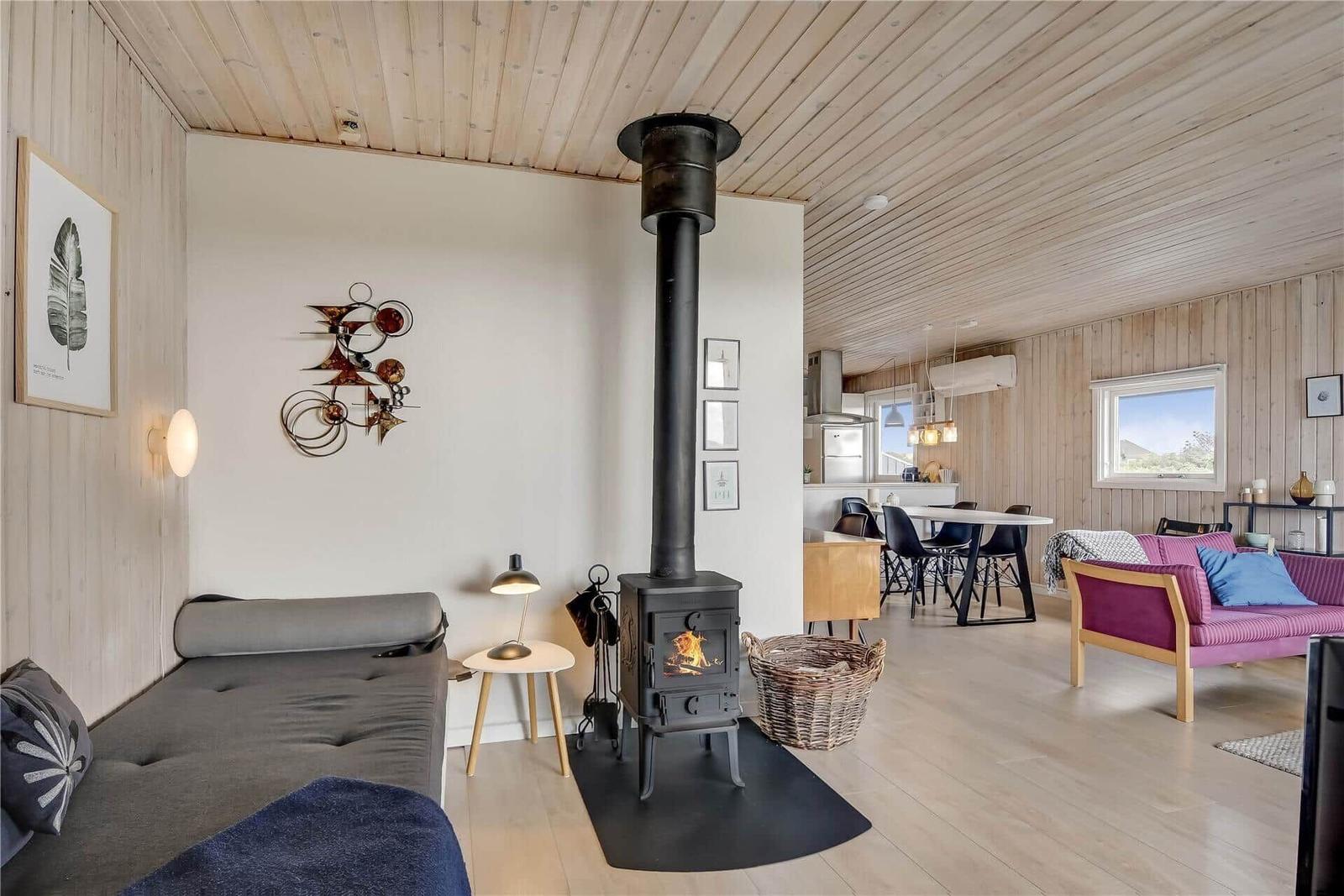 Wohnraum mit Kaminofen, Sofa und Essbereich. Holzwände und -decke.