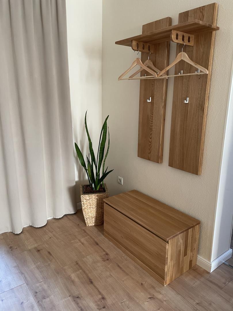 Holzgarderobe mit Haken und Ablage, Sitzbank und Pflanze neben Fenster