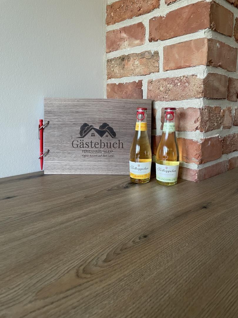 Gästebuch und zwei Flaschen auf Holztisch neben Backsteinwand.