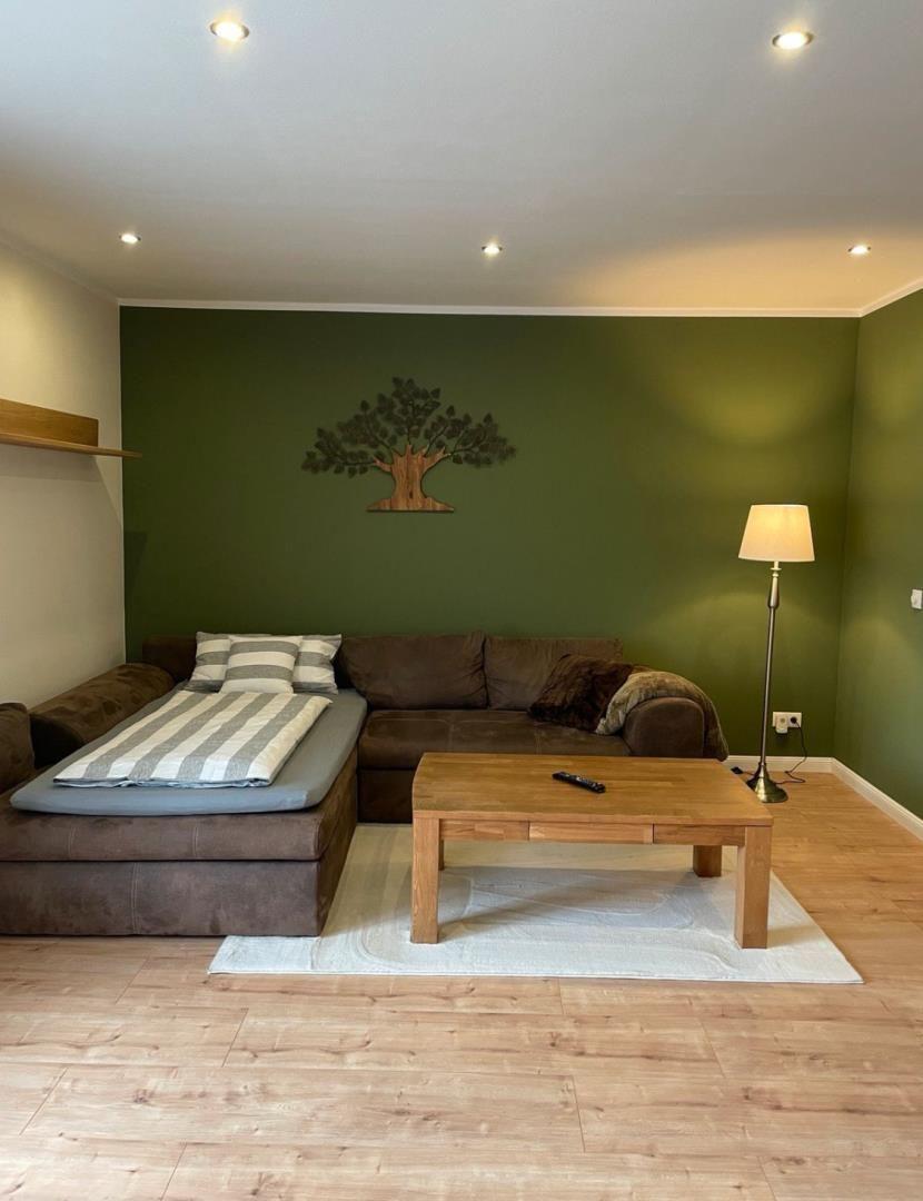 Wohnzimmer mit Sofa, Holztisch und grüner Wand mit Baumdekoration.