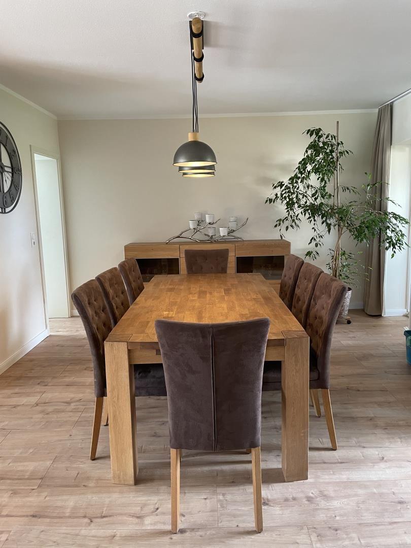 Esszimmer mit Holztisch, sechs Stühlen und Pflanze. Hängelampe und Sideboard sichtbar.