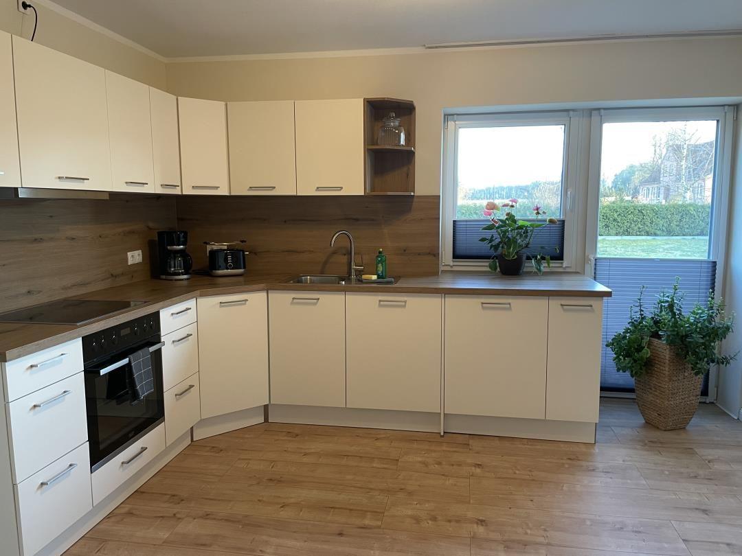 Küche mit hellen Schränken, Holzoberfläche und Fensterblick auf Grünfläche.