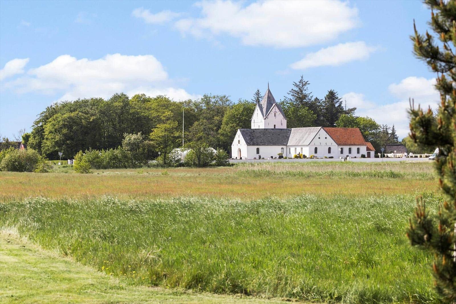 Weißes Kirchengebäude mit Turm steht in grüner Landschaft unter blauem Himmel.