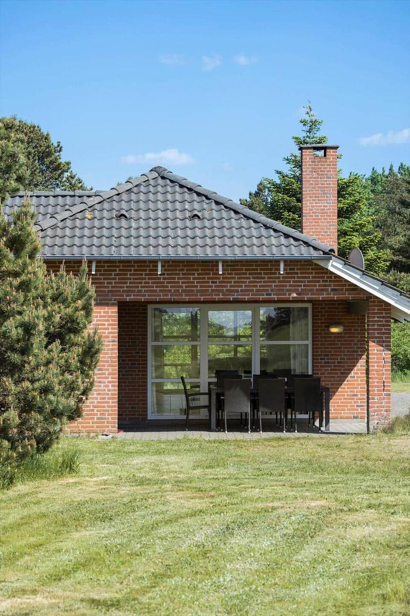 Ein kleines Haus mit Terrasse, Sitzgruppe und Grillplatz im Garten.