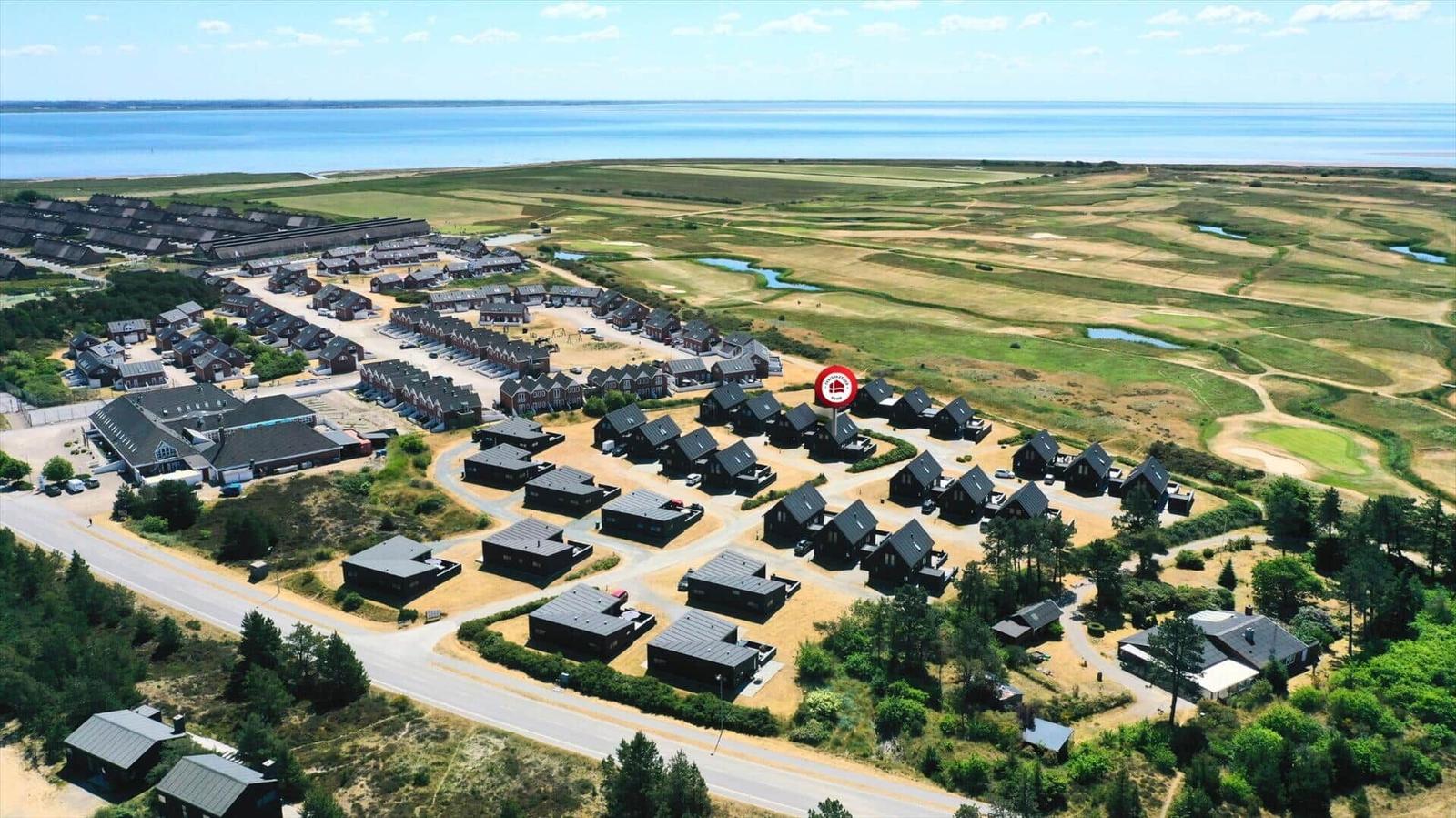Aerial view of holiday homes near a large body of water and green fields.