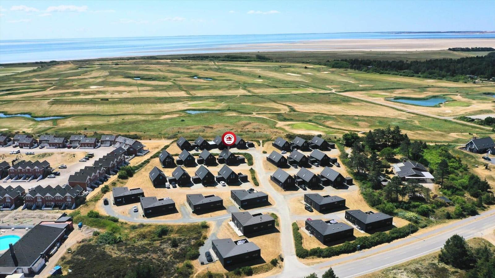 Luftbild von Ferienhäusern mit Golfplatz und Strand im Hintergrund.