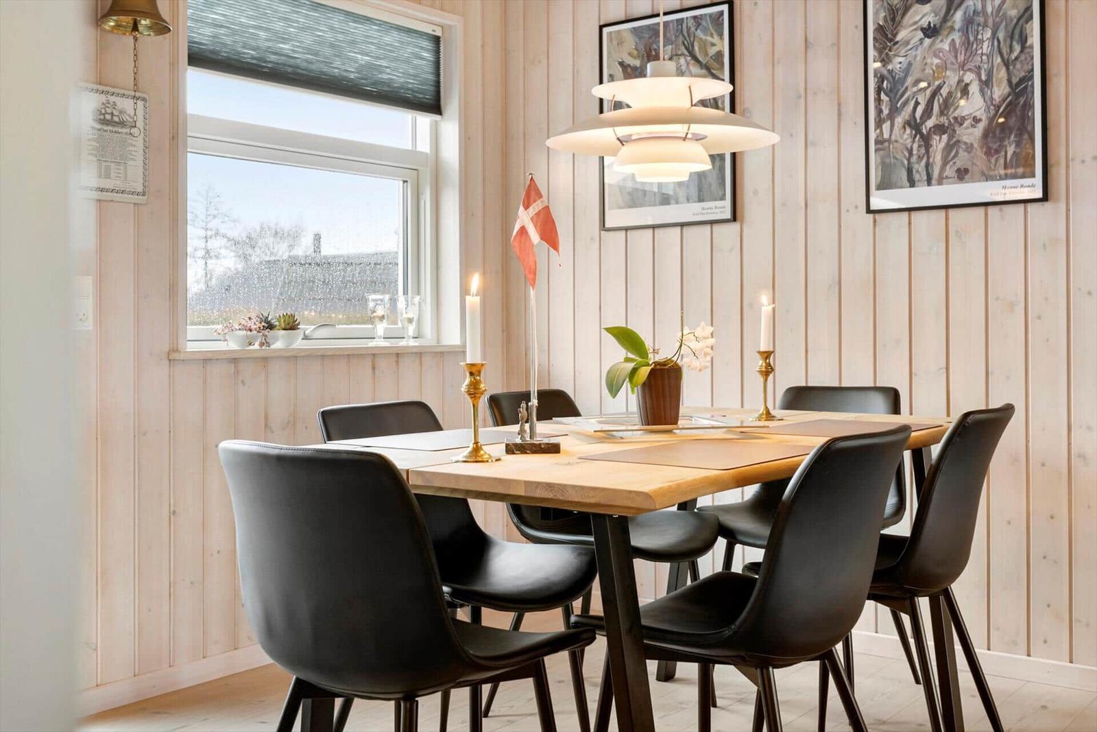Esszimmer mit Holztisch, schwarzen Stühlen und dänischer Flagge. Wandverkleidung aus Holz und Fenster mit Blick.
